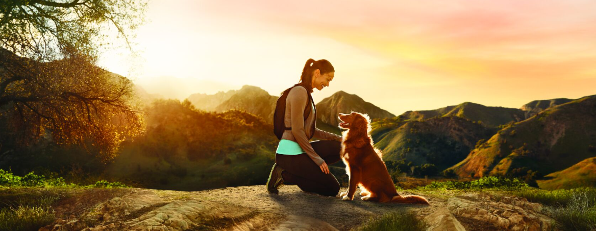 nő kutyával a hegyekben kirándul naplementekor
