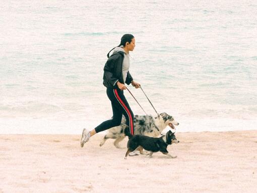 Fiatal nő fut két kutyájával tengerparton